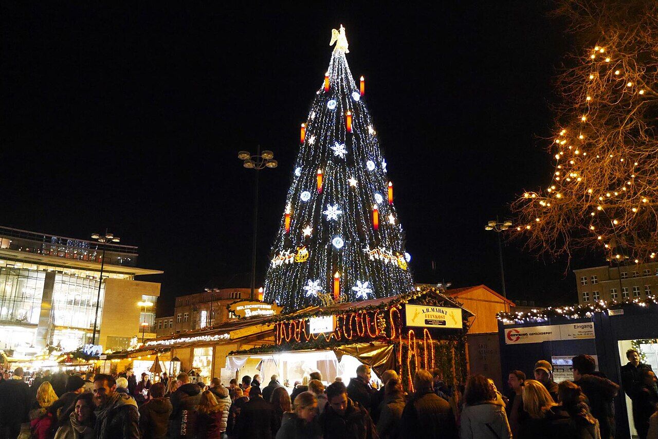 Riesiger beleuchteter Weihnachtsbaum über den Buden der Dortmunder Weihnachtsstadt auf dem Hansaplatz bei Nacht