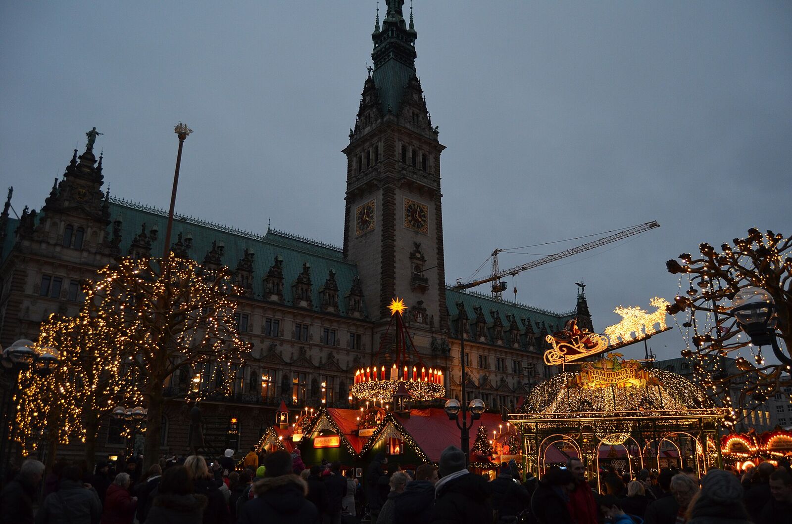 Weihnachtsmarkt auf dem Hamburger Rathausmarkt in der Dämmerung mit beleuchtetem Eingangstor, Lichterbäumen und Rathausturm