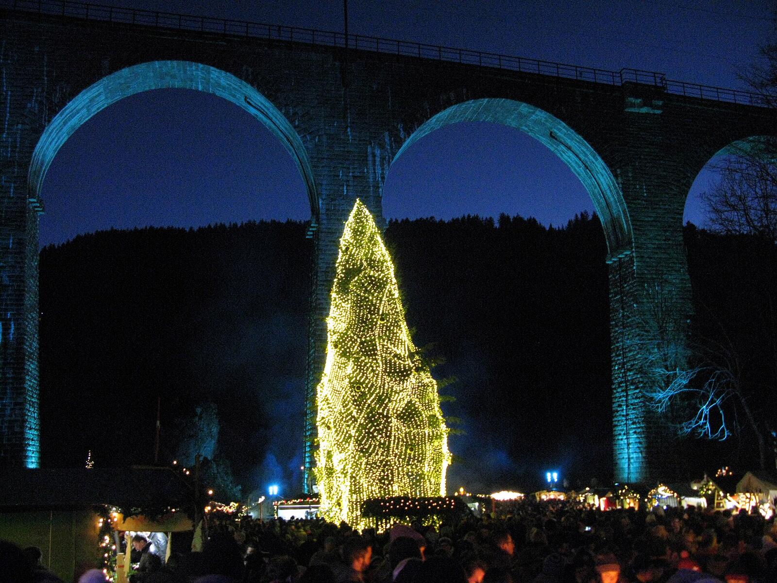 Weihnachtsmarkt unter dem angestrahlten Eisenbahnviadukt in der Ravennaschlucht mit leuchtendem Lichterbaum zur blauen Stunde